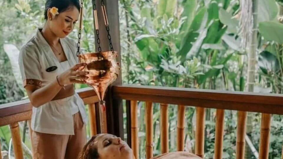 A practitioner at Ubud Nyuh Bali Resort uses the Shirodhara treatment for relaxation on a retreat participant.