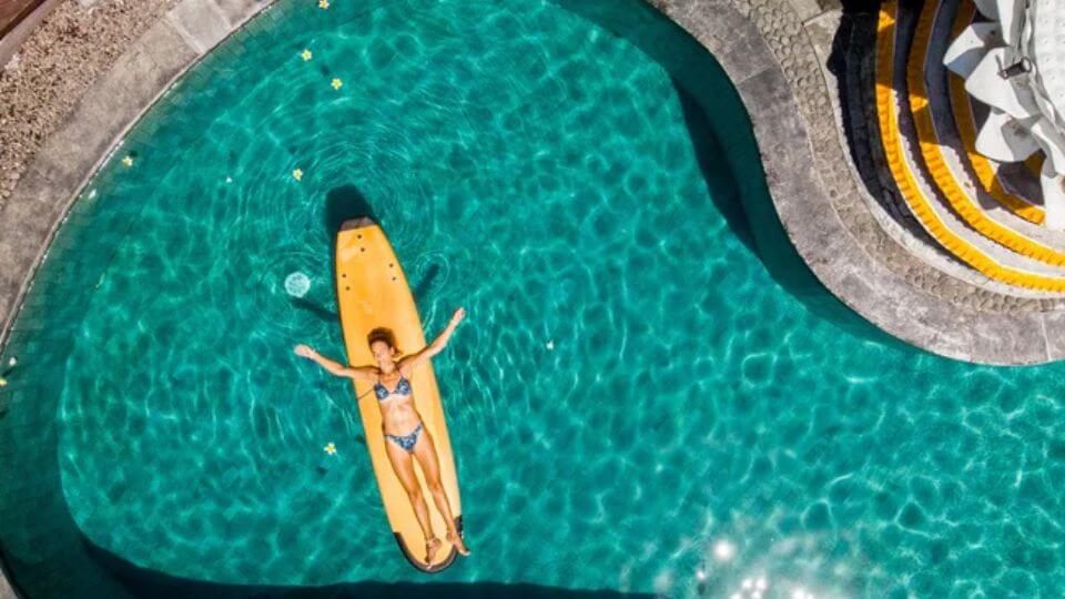 An overhead view of a person lying on their back on a surf board in the swimming pool at Surf and Yoga Bali.