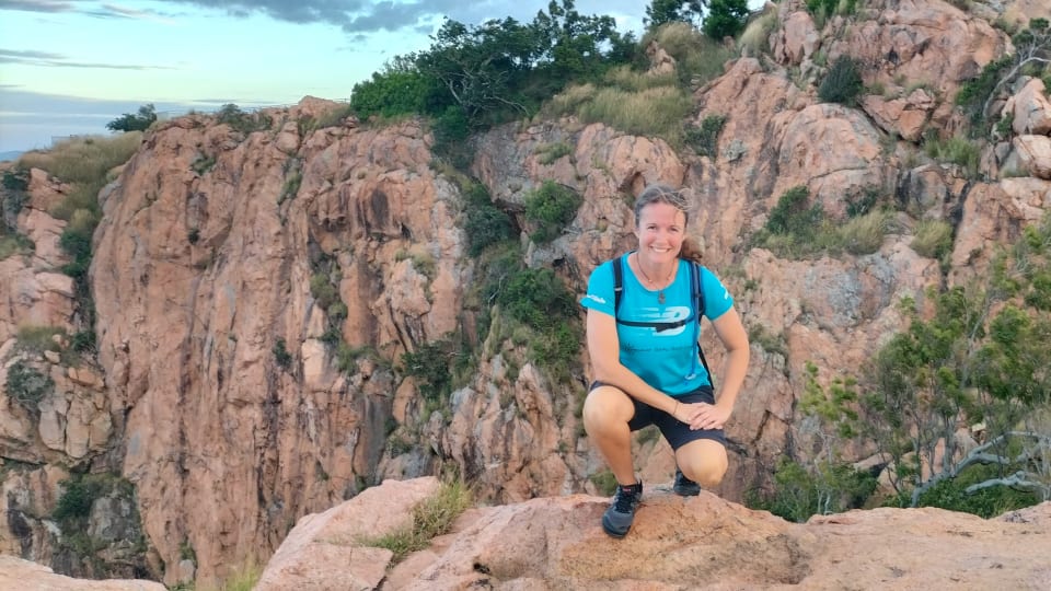 Elly crouches down on a rock at the top of Castle Hill in Townsville during her first hike in the Mesa Trail II barefoot trail shoes from Xero Shoes.