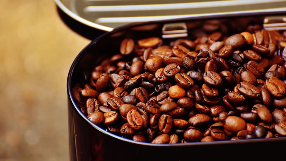 An open tin of whole coffee beans.