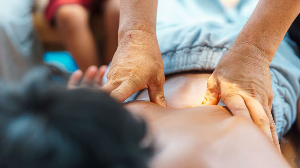 A person applies pressure through their thumbs onto specific points on another person's back.