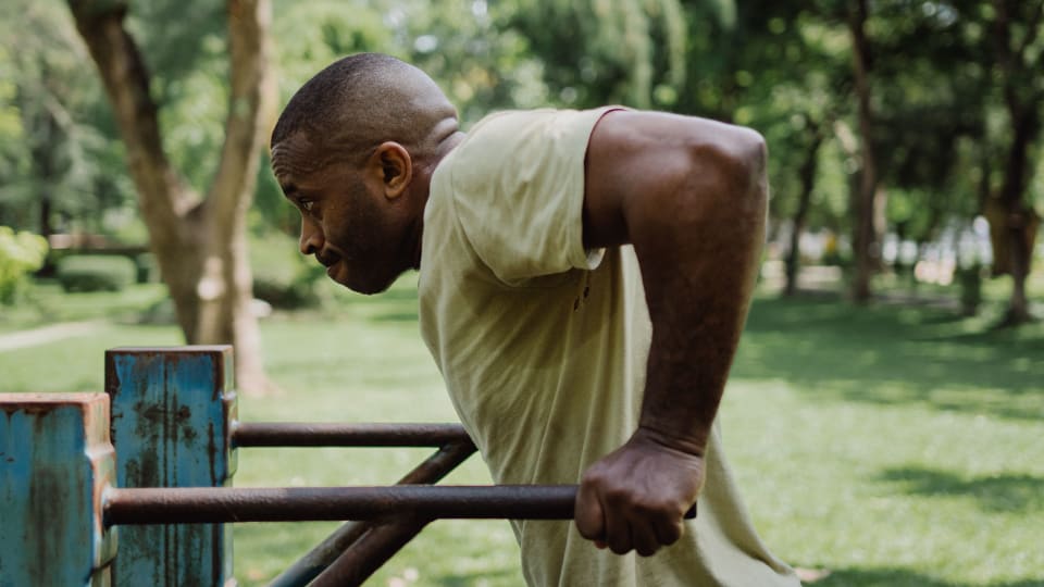 A person does a dip on parallel bars at an outdoor gym.