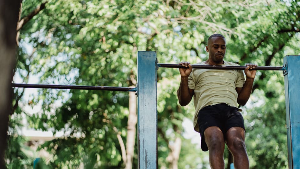 A person does a pull-up on a bar in an outdoor fitness setting.
