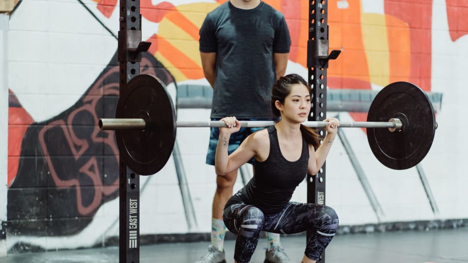 A person doing a barbell back squat, one of the four core lifts in a streetlifting workout.
