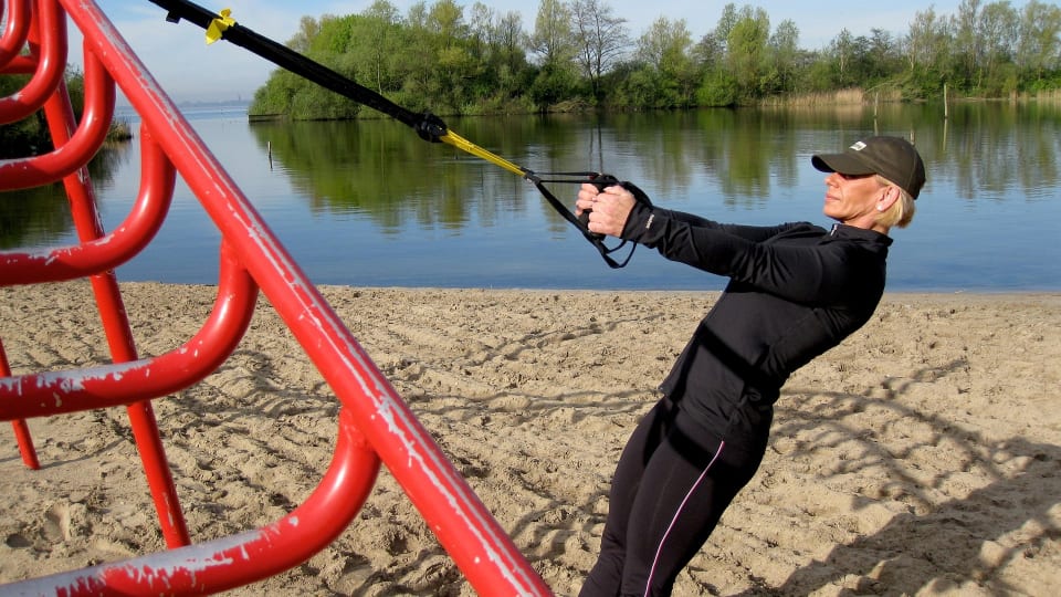 A person in a start position for suspension training exercises in a beautiful lakeside environment.