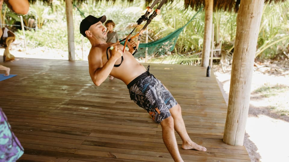 A person performs a row exercise on a suspension trainer, anchored inside a hut.
