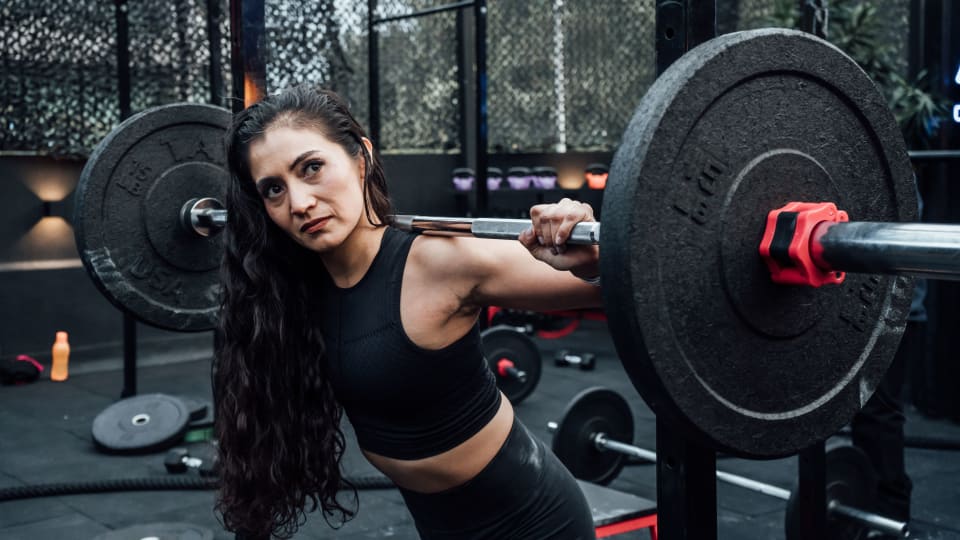 A person prepares for a barbell back squat with the bar across the back of their shoulders.