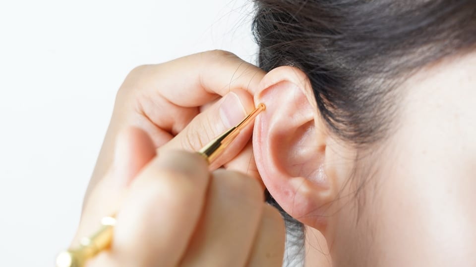 A person uses an acupressure pen on the inside of another person's ear.