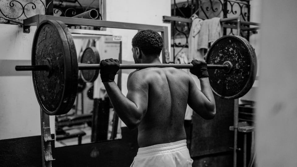 A person with a weighted barbell on their back in a gym.