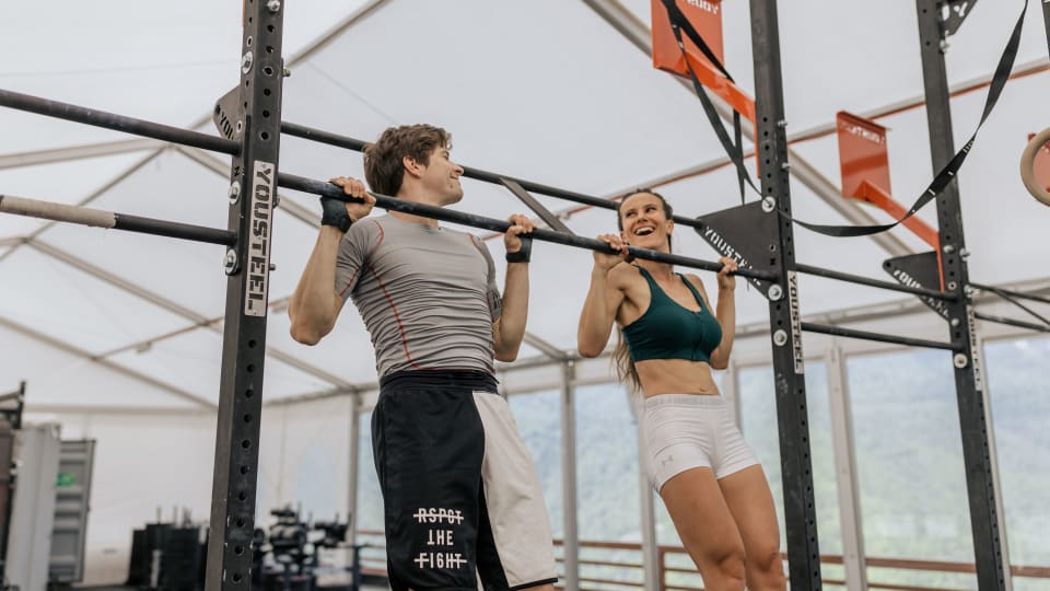 Two people train pull ups together in a gym.