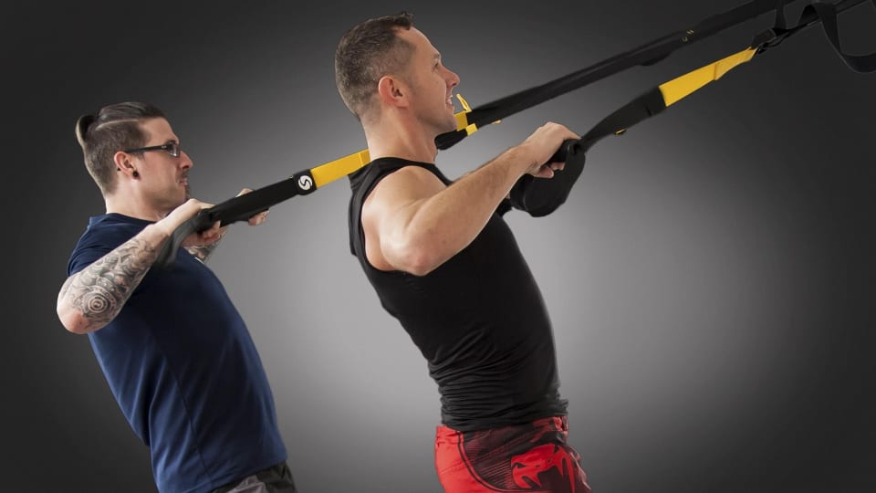 Two people work side by side on suspension trainers, performing a row movement.