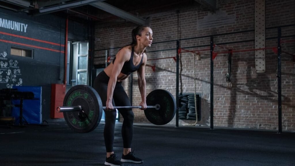 A person holding a barbell with an overhand grip in front of their body, just above their knees.