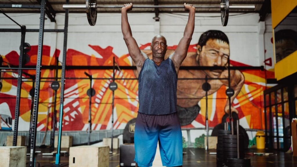 A person holds a barbell overhead in a gym setting.