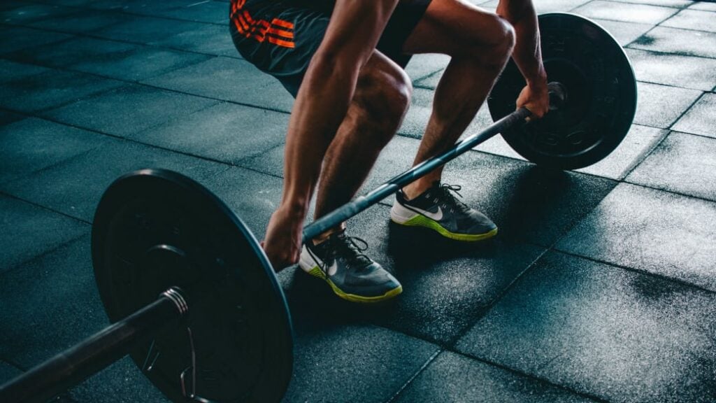 A person squats down, holding onto a barbell, preparing for a deadlift, an excellent compound exercise.