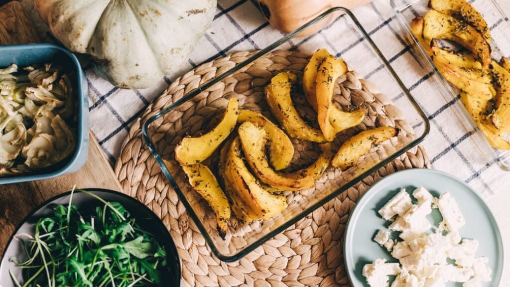Various ingredients or side dishes, including pumpkin, greens, mushrooms and white cheese on plates on a table.