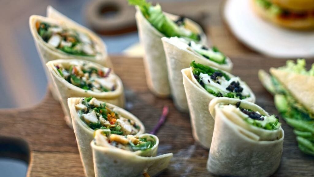 Vegetable rollups or wraps lined up on a wooden chopping board.