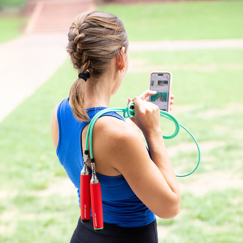 View of the back of a person holding a Crossrope over their shoulder with one hand and their phone in the other.