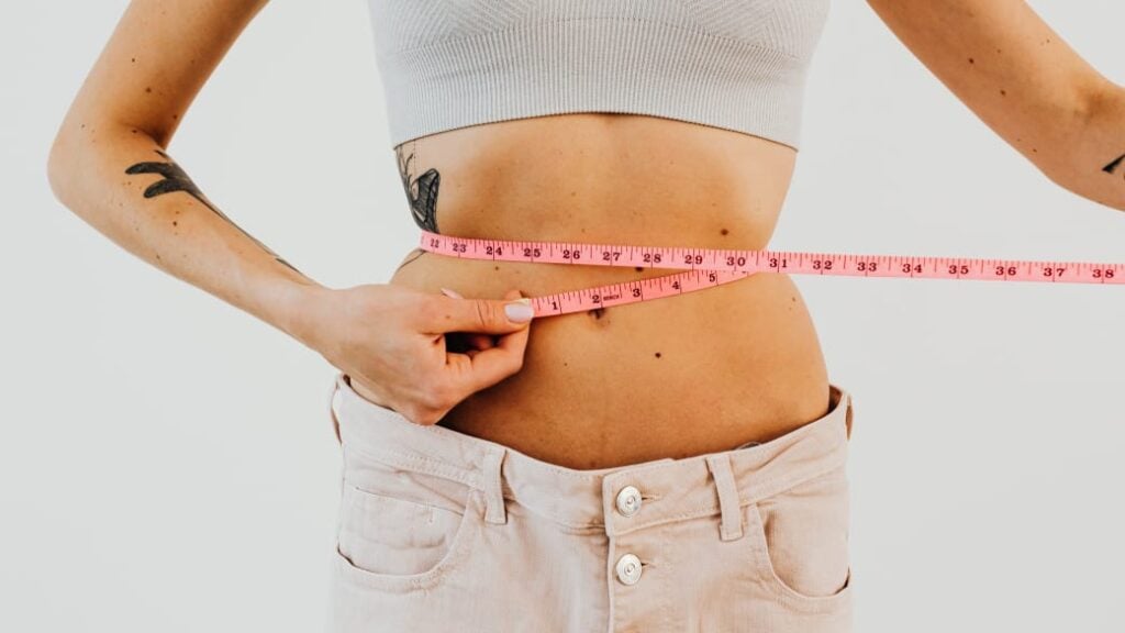 A person measures their waist with a tape measure.