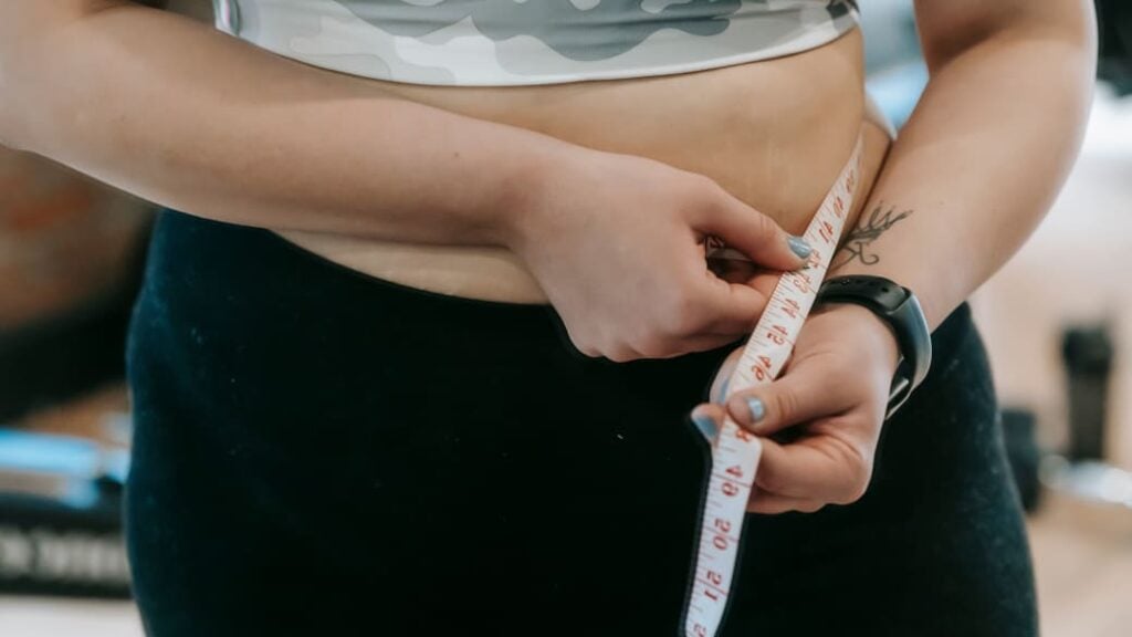 A person wraps a measuring tape around their bare midsection.