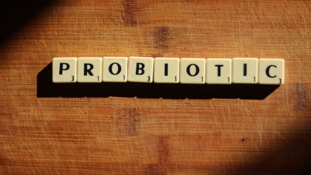 the word probiotic made with scrabble pieces, sitting on a wooden surface.
